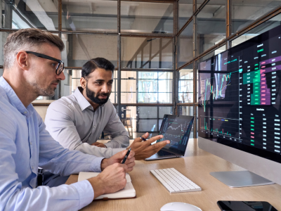 Two men seated at a desk reviewing data on a large computer monitor