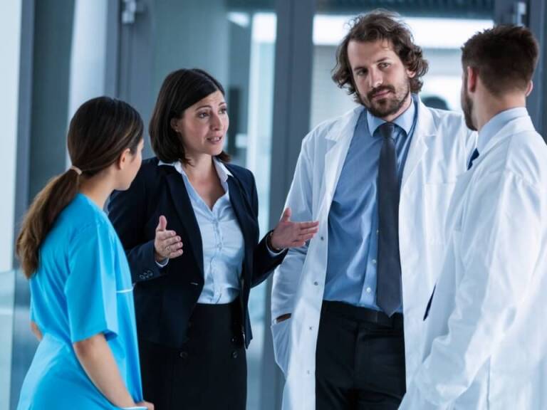 Three medical professionals in uniform speaking to woman in business attire