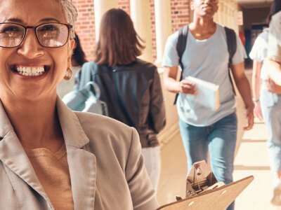 Closeup of school principal smiling in a hallway, while students walk in the background.