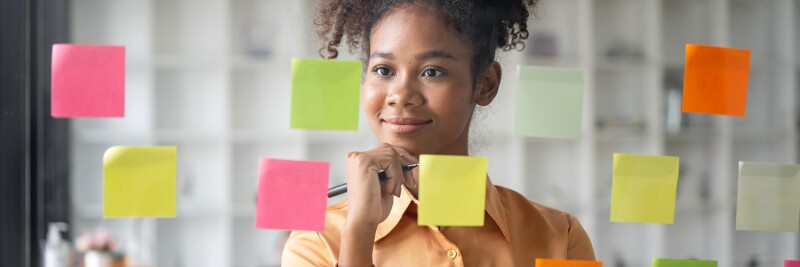 Young businesswoman using sticky notes on glass wall