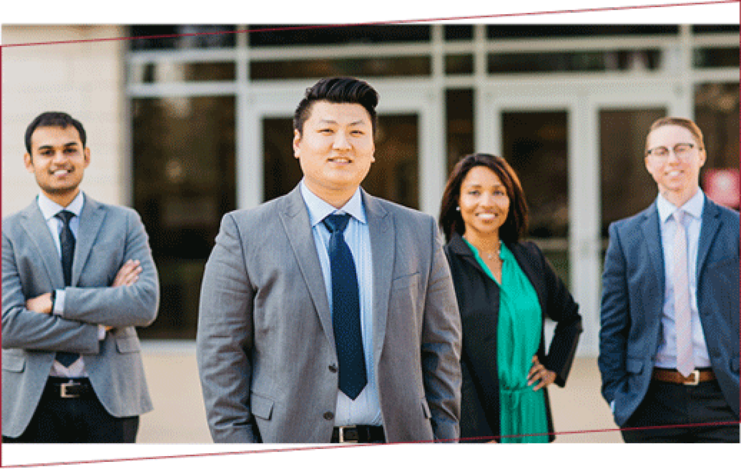 group of four business professionals outside a building, smiling at the camera