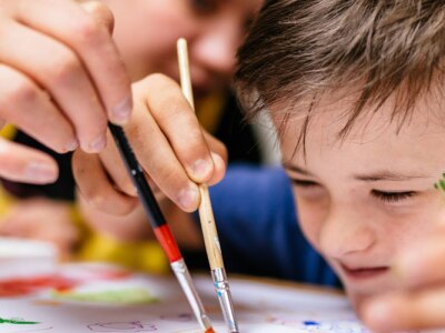 Young female teacher explain, talk at desk with an autistic schoolboy.