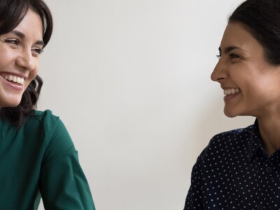 Two women having a conversation seated at desk in workplace.