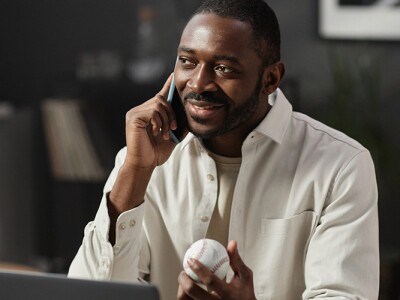 Man speaking on the phone in his office holding baseball