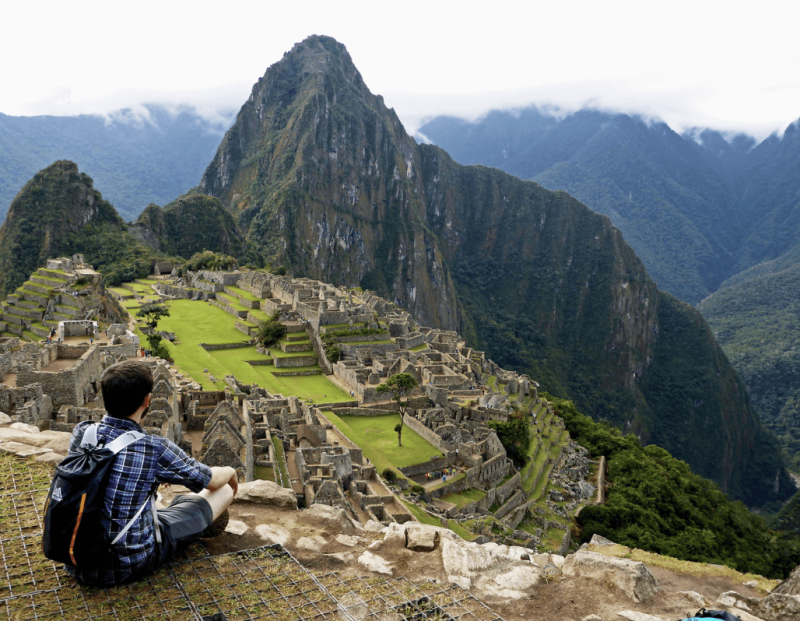 Man in backpack seated on cliff overlooking mountains