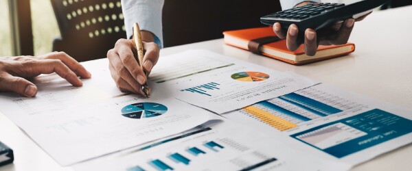 Man stands over financial papers while holding a pen and calculator