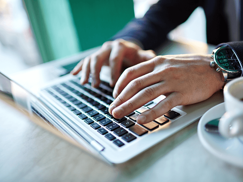 Hands typing on laptop next to coffee cup