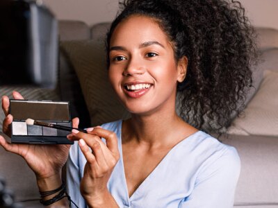 Smiling woman holding a makeup palette while recording her video for blog..
