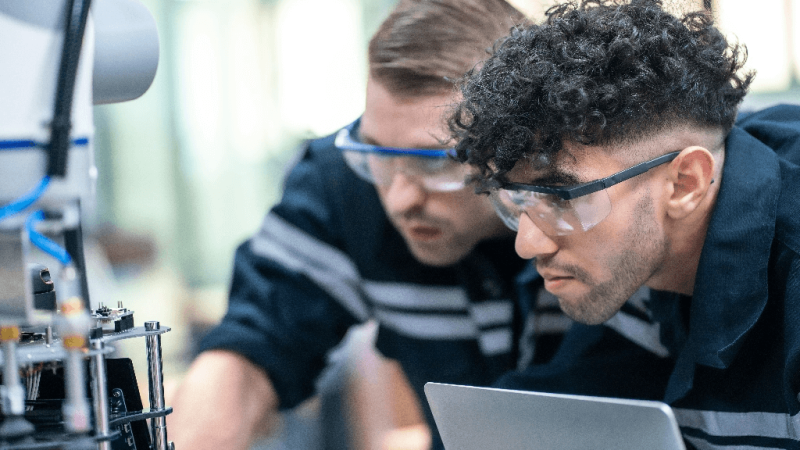 Two mechanical engineers in goggles looking closely at a machine