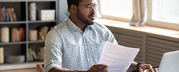 Serious-looking professional using laptop, holding document and pen