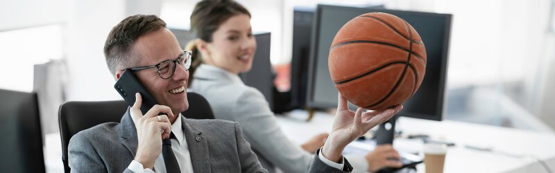 A sports agent on the phone in an office setting with a potential client while holing a basketball
