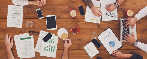 Documents and devices on a table with hands of employees