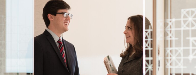 Two Marquette students speak to one another in business attire in a glass office space