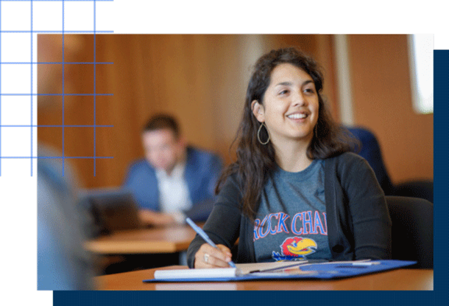 A female KU student is smiling while writing notes in a notebook.