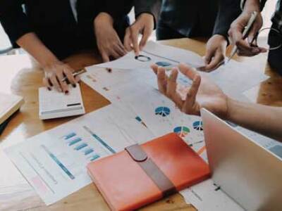 Four people in discussion around a table piled with papers, books and a laptop