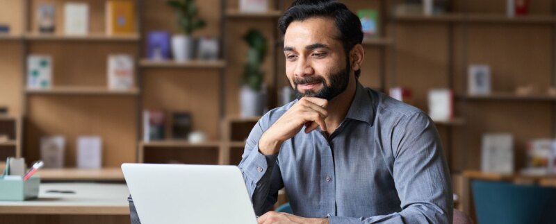 Smiling man reading the screen on his laptop in a library