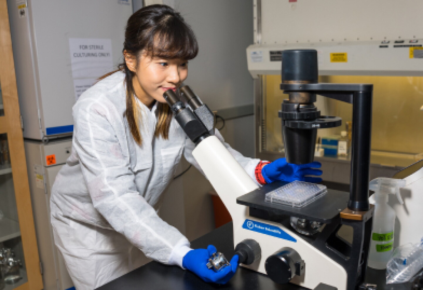 Close-up of a female CWRU biomedical engineering student reviewing sample through a microscope.