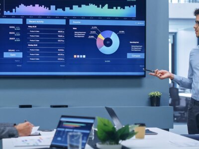 Latin Businessman Talks, Uses Wall TV to Show Company Growth with Big Data Analysis, Graphs, Charts, Infographics.