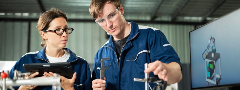 Two mechanical engineers examine a component using precision measuring tools.