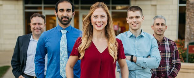 One woman and four men standing in a line smiling