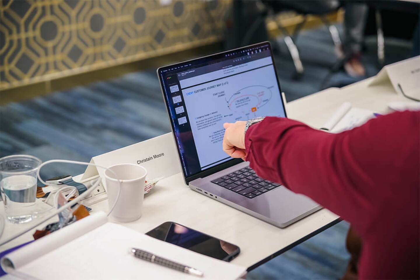 Hand pointing to a laptop on a table