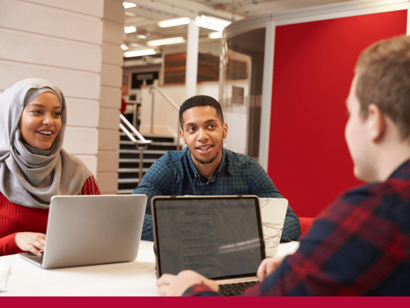 Two men and woman seated collaborating with laptops