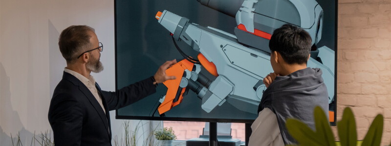 Two men review a design for a game device on a big screen in an office.