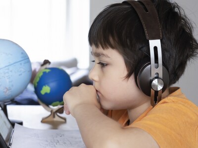 Boy in yellow shirt watching laptop globes in the background