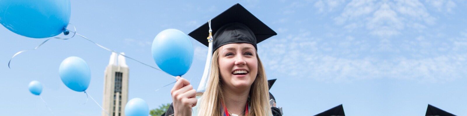 Graduate in cap and gown holding blue balloons