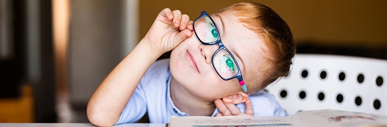 Young child with blue shirt and glasses tilting his head