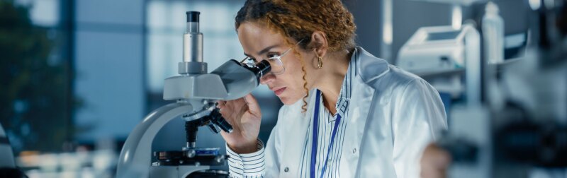 A female Biomedical Engineer in a lab testing Biological Samples under a microscope.