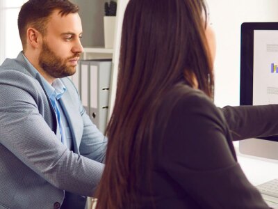 Two businesspeople analyzing data charts while looking at financial metrics on computer screen.