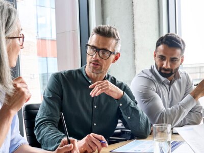 Diverse international executive business partners group discuss report at boardroom meeting table.