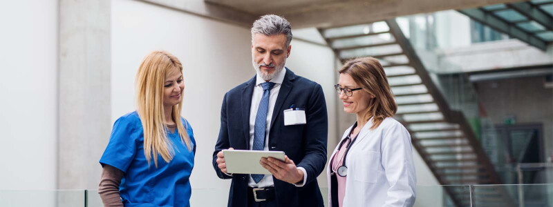 A professional in a suit shows a doctor and a nurse information on a tablet.