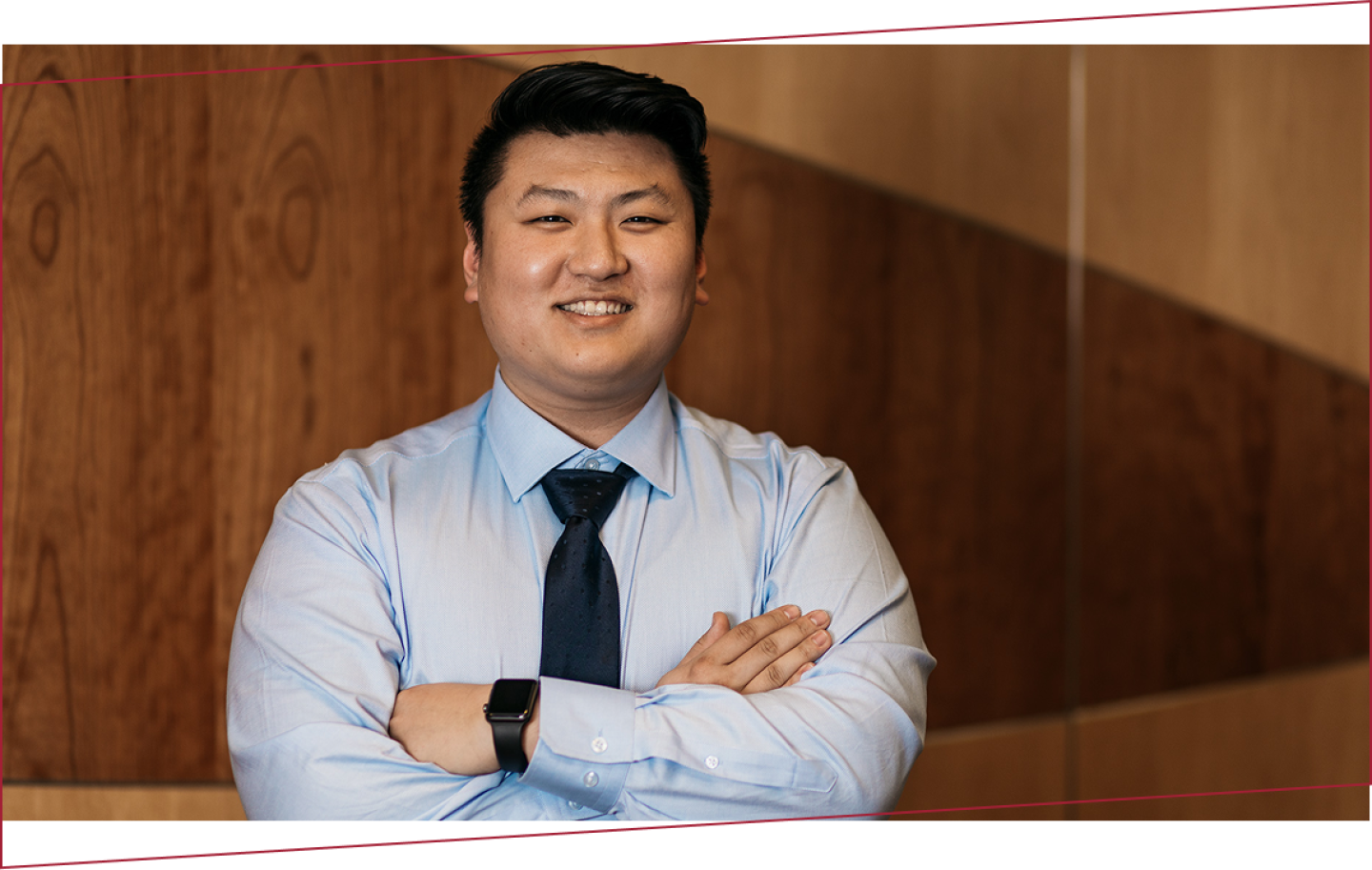 Smiling person in a light blue dress shirt and dark tie, arms crossed.