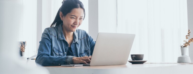 Adult in jean shirt works on laptop at kitchen table
