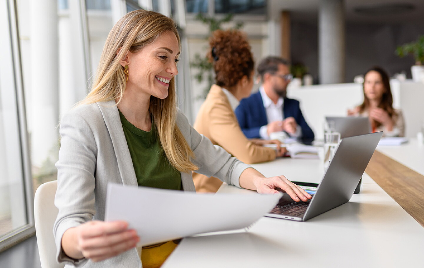 woman sitting in a conference room looking comparing paperwork to her screen