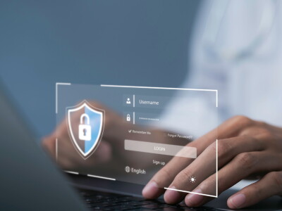 Close-up image of a doctor's hands typing on a laptop. A digital image depicts a login screen.
