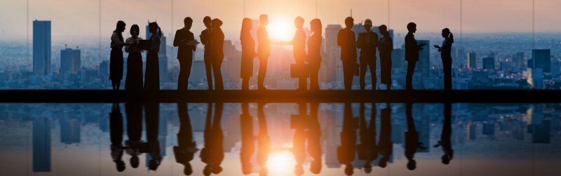 Silhouettes of business professionals standing in a high-rise corporate office as the sun rises.