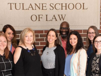 Tulane Law professionals and students stand below the Tulane School of Law sign.