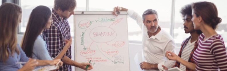 five students around white board taking notes while teacher in white shirt presents graph