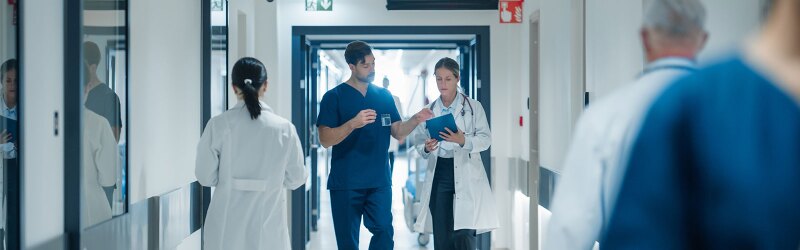 A doctor and a nurse are discussing an upcoming surgery while walking through a busy hospital hallway.