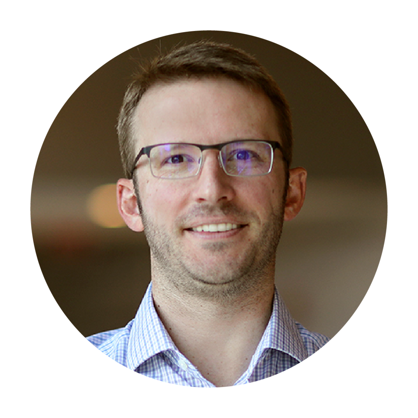 Headshot of Ted Unger, smiling and wearing glasses and a light blue collared shirt, photographed against a softly blurred indoor background.