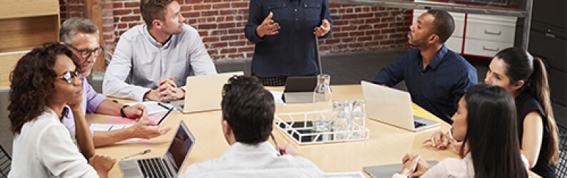 people in a meeting around a table with laptops