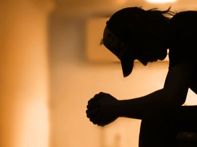 Silhouette of a young man sitting in a dark hallway with his arms crossed on his knees.