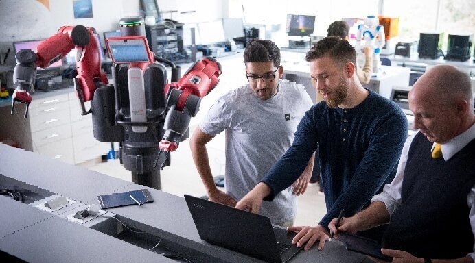 Three engineers operating robotic arm with laptop computer