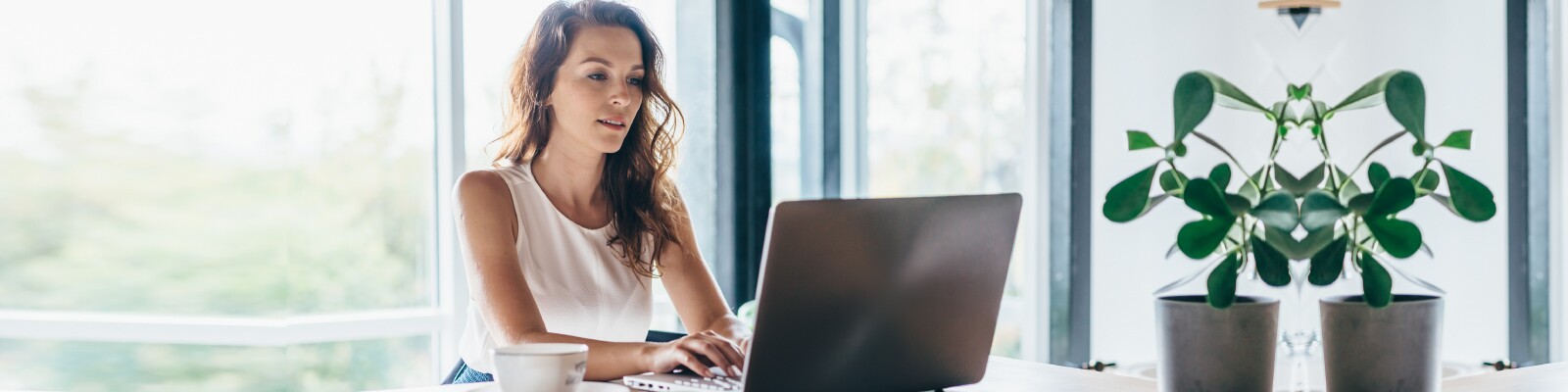 Woman with wavy hair sits in her home working on laptop