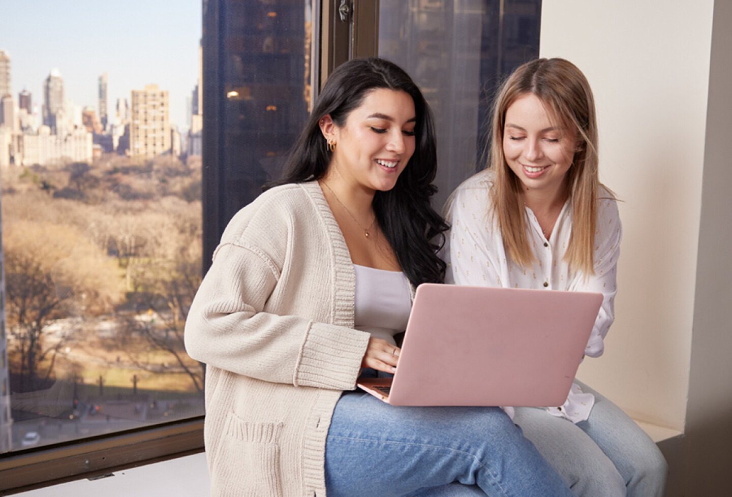 Students working together on a laptop while sitting on a windowsill