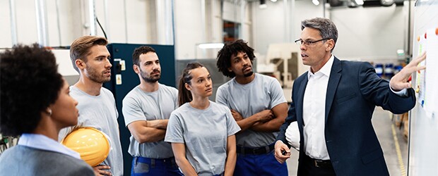 professor standing in front of whiteboard speaking with 5 students
