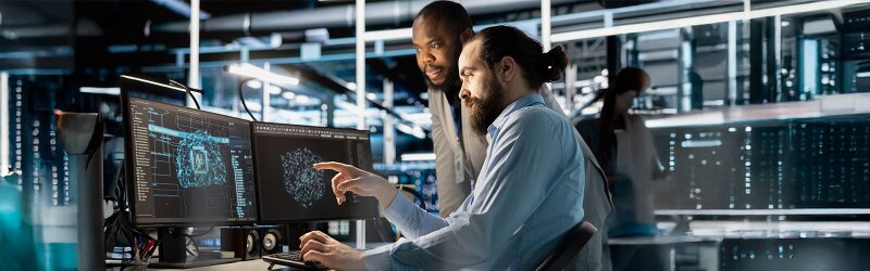 two men looking at double monitors displaying AI images